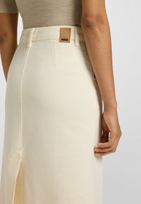 Gonna di jeans beige con spacco laterale, dotata di una toppa in pelle con logo sul girovita. Tessuto morbido e design aderente.