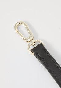 Sangle en cuir noir avec un clip en métal doré. Texture lisse avec un détail de couture le long des bords. Le clip présente un mécanisme à ressort sécurisé.