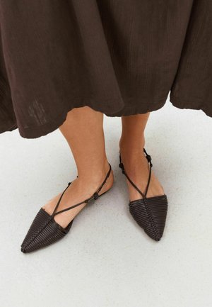 Spitz zulaufende dunkelbraune gewebte Lederflats mit dünnen Knöchelriemen, getragen zu einem braunen Midirock auf heltem Boden.