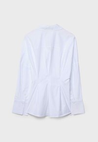 Bela srajca z dolgimi rokavi z gumbi, s koničastim ovratnikom, nabranim hrbtom in zanko na manšetah, prikazana od zadaj na enostavni podlagi.