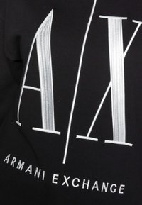 Černá mikina s výrazným bílým vyšitým logem "A|X" a nápisem "ARMANI EXCHANGE" ve spodní části. Hladká textura látky.