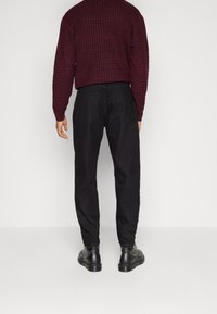 Tumman viininpunainen neulepaita, jossa on tekstuurikuvio, yhdistettynä mustiin housuihin. Jalkineina mustat nauhakenkä bootsit, joissa on sileä pinta.