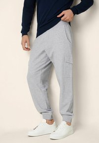 Grå bomullsträningsbyxor med elastiska muddar och sidofickor, kombinerat med vita sneakers. Designen har en avslappnad passform och mjuk textur.