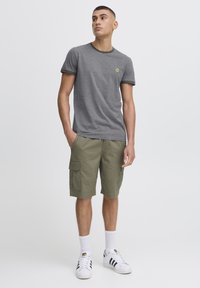 Grå kortærmet t-shirt med mørkegrøn krave, parret med olivengrønne cargo shorts med sidelommer, og hvide sneakers med sorte striber.