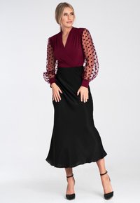 Langes schwarzes Kleid mit tailliertem Oberteil und ausgestelltem Rock. Das burgunderfarbene Oberteil hat durchsichtige, gepunktete Puffärmel. Glatte Textur im gesamten Kleid.