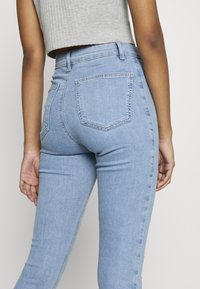 Jeans de mezclilla de color azul claro, de cintura alta, con bolsillos traseros y una textura ligeramente desgastada. Acabado suave, silueta ajustada.