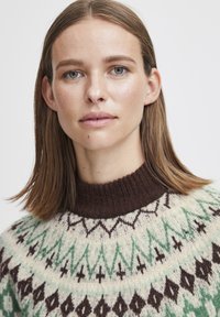 Knit sweater with a high brown collar, featuring a geometric pattern in green and brown on a cream background.