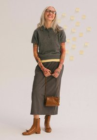 Camisa polo de lana gris con una camiseta amarilla debajo, falda gris, botas de tobillo de cuero marrón y un pequeño bolso de mano marrón texturizado.