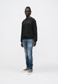 Μαύρο φούτερ με λογότυπο "DIESEL", μπλε τζιν παντελόνι, γκρι αθλητικά παπούτσια. Ομαλό ύφασμα, χαλαρή γραμμή και διακριτική υφή στο λογότυπο.