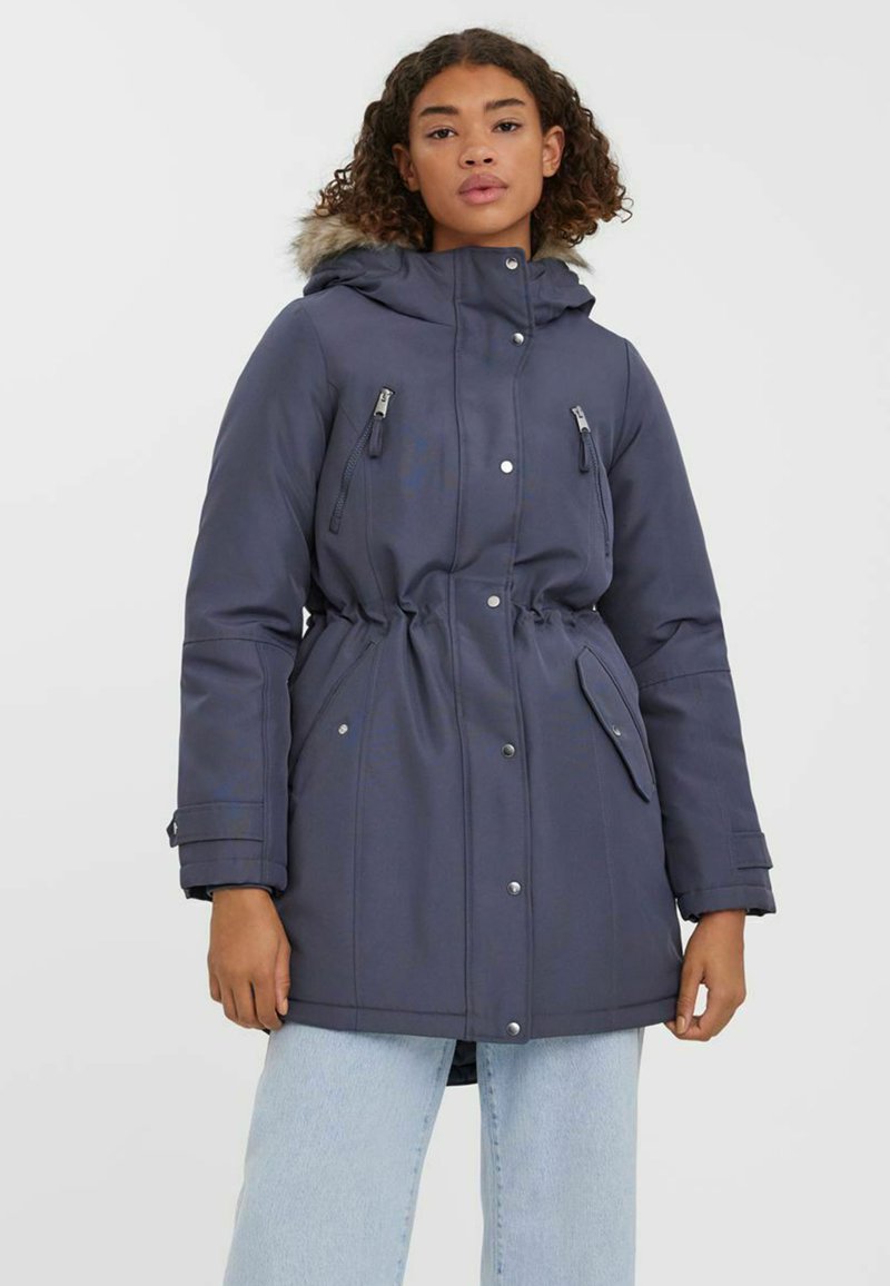 Krajša temno modra parka s podlogo iz krzna in kapuco, z elastičnim pasom, zadrgo v žepih in pritisnimi gumbi. Ima gladko zunanjost in dolge rokave.