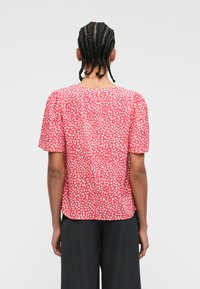 Κοντομάνικο τοπ σε κοραλί χρώμα με λευκές κηλίδες, μαλακό ύφασμα, στρογγυλή λαιμόκοψη και ελαφριά συγκέντρωση στις ραφές των ώμων.