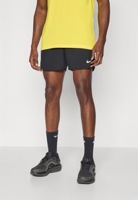 Nike svarta shorts med en vit logotyp, kombinerat med svarta träningsstrumpor med en liten vit logotyp och svarta sneakers med texturerad detalj.