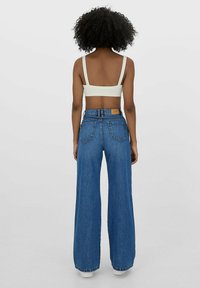 Laaja jalka siniset farkut korkealla vyötäröllä, joissa on kaksi takataskua ja ruskea nahkatägi vyötäröllä. Vaahtoava vaaleanvärinen lyhyt toppi.