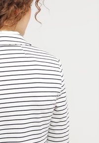 Chemise rayée blanche et marine, dotée d'un col classique, d'une texture côtelée et d'une coupe droite, présentée de dos avec des coutures visibles.