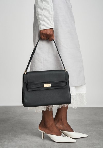 Bolsa de couro preta com uma forma estruturada, ferragens douradas e uma alça superior. Características notáveis incluem um flap frontal e costura de destaque.