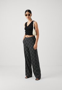 Svart cropped topp med rynkede detaljer, parret med vide bukser med mønster i sort og hvit diamantdesign. Tilbehør inkluderer en beige håndveske og solbriller.