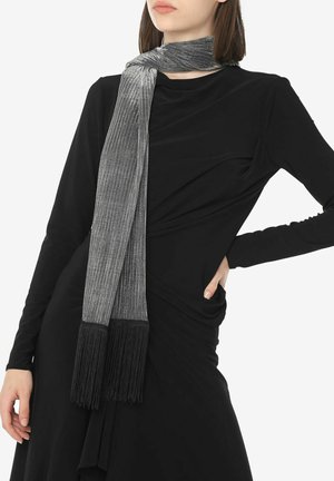 Écharpe argentée texturée avec des franges noires à chaque extrémité, portée sur un haut noir. Le tissu a une finition brillante et métallique et tombe tout droit.