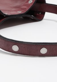 Bordowa skórzana torebka o gładkiej fakturze, z metalowymi zatrzaskami i wzmocnionym paskiem dla większej trwałości.