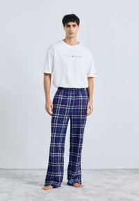Biely bavlnený tričko s logom "TOMMY HILFIGER". Modré kárované pyžamové nohavice s červenými a bielymi akcentmi, so širokým elastickým pásom.