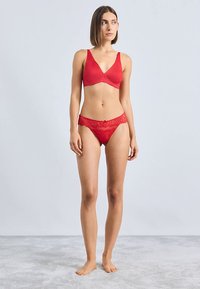 Rotes BH- und passendes Spitzenhöschen-Set. Der BH hat eine glatte Oberfläche mit gezackten Kanten; das Höschen ist mit Spitzendetails und einer Schleifenakzent versehen.