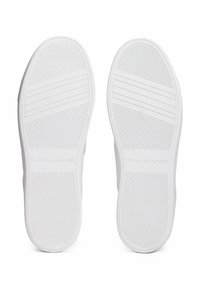 Sole di sneakers bianche con gomma testurizzata, dotate di scanalature orizzontali e verticali per una migliore aderenza. Logo "TOMMY HILFIGER" impresso su una delle suole.