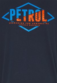 Marineblå t-shirt med kraftig orange och blå text: "PETROL" och "SEARCHING FOR ADRENALINE" med en diamantkonturdesign.