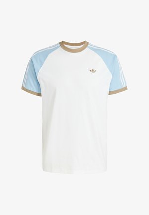 Camiseta blanca con mangas raglán azul claro, cuello de canalé marrón y tres rayas verticales blancas en los hombros. Presenta un pequeño logo dorado.
