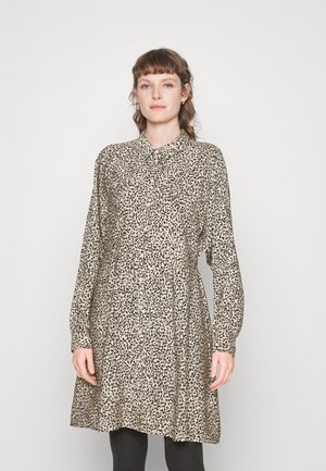 Vestido camisa bege com um padrão de manchas pretas, mangas longas e gola com botões; ajuste descontraído com cintura franzida, feito de tecido leve.