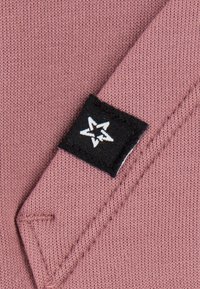 Tissu tricoté mauve avec une étiquette noire visible ornée d'un motif d'étoile blanche, et une surface propre et texturée.