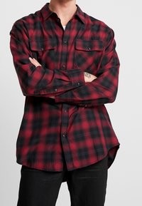 Röd och svart rutigt flanellskjorta med långa ärmar, knappstängning framtill och två bröstfickor. Har rundad nederkant och mjuk textur.