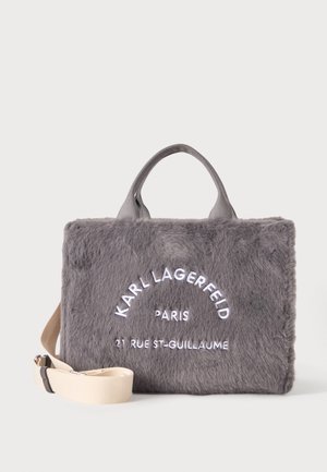 Grå blød kunstig pels håndtaske med korte håndtag og aftagelig beige skulderrem, med hvid Karl Lagerfeld Paris mærkning foran.