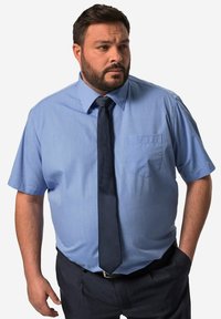 Camisa de dress de manga corta en azul claro con un bolsillo en el pecho, combinada con una corbata de color azul marino oscuro y pantalones oscuros. Textura de tela suave.