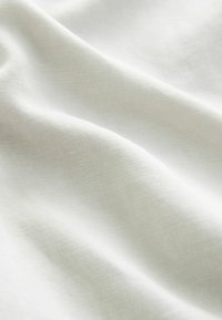 Összefonódott felületű, lágy esésű, textúrált off-white vászonanyag, amely finom redőket és sima felületet mutat.