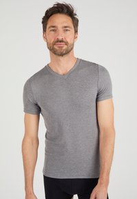 Maglietta grigia a maniche corte con scollo a V, realizzata in un tessuto liscio, con un design aderente e cuciture minime, indossata con pantaloni neri.
