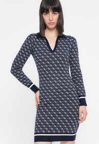 Abito in maglia a motivo navy con scollo a V, maniche lunghe e polsini e orlo bianchi a contrasto. Design geometrico in tonalità più chiare.