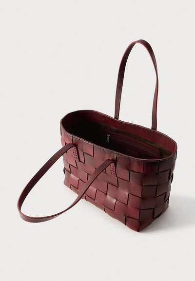Σκούρα κόκκινη δερμάτινη τσάντα ώμου με υφαντή υφή, ανοιχτό πάνω μέρος που δείχνει εσωτερική τσέπη με φερμουάρ και δύο μακριές λουρίδες ώμου.
