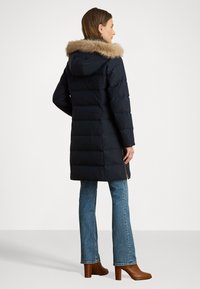Jūras spēku puffer jaka ar mēteli, kas odere ir no kažokādas, horizontālām quiltēm un sānu rāvējslēdzēja akcentiem. Nēsāta virs platām džinsām un ar papēžiem.