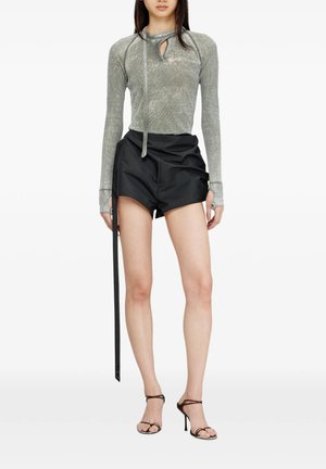 Donna che indossa un top grigio a maniche lunghe con fori per i pollici, pantaloncini neri a vita alta con cintura estesa e sandali neri con tacco alto e cinturini.