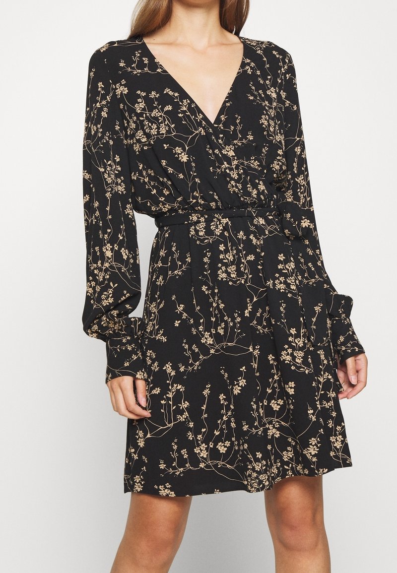 Musta, pitkähihoinen mekko syvällä V-kaula-aukolla, jossa on beige kukkakuosi. Sisältää sidottavan vyötäröyksityiskohdan.