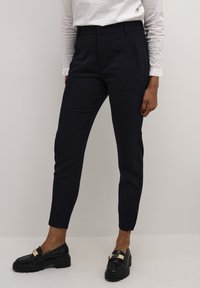 Navy tapered trousers with a smooth texture, side pockets, and a sleek design, paired with black loafers featuring a gold accent.