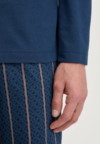 Blauw langemouwen shirt met ribbelstructuur, gecombineerd met gebloemde blauwe broek met grafisch ontwerp en verticale strepen in oranje.