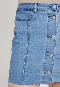 Jupe boutonnée en denim bleu clair à coupe droite, avec un ourlet brut, cinq boutons métalliques et des poches latérales avant.