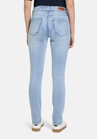 Jasnoniebieskie wąskie dżinsy o gładkiej teksturze denimu, z pięcioma kieszeniami i brązową skórzaną naszywką na tylnej części pasa.