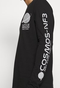 Svart långärmad t-shirt i bomull, med vit grafisk text och bilder av en planet på framsidan och en design på ärmen.