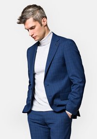 Niebieski garnitur w kratę o smukłym kroju, noszony na jasnoszarym golfie. Teksturowany materiał i subtelne detale podkreślają całość stylizacji.