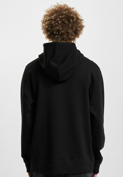 Black hoodie with a soft texture, adjustable hood, and long sleeves. Features visible seams and a relaxed fit. No graphic designs.