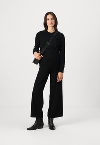 Black knit sweater with long sleeves, paired with high-waisted wide-leg black trousers. Black heeled ankle boots, crossbody bag with logo strap.