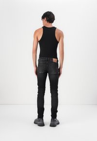 Black tank top paired with dark gray skinny jeans. Notable details include a rear patch label and textured fabric on the jeans. Footwear is gray.