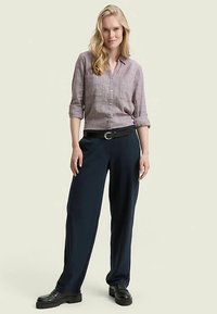 Lichtpaarse overhemd met knopen en opgerolde mouwen, gecombineerd met donkerblauwe broek met wijde pijpen en een zwarte riem. Soepele textuur en een ontspannen pasvorm.