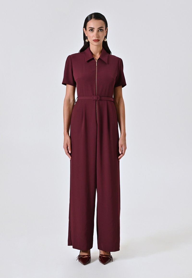 Tuta bordeaux in tessuto leggero, con maniche corte, zip frontale, cintura in vita e pantaloni a gamba larga.
